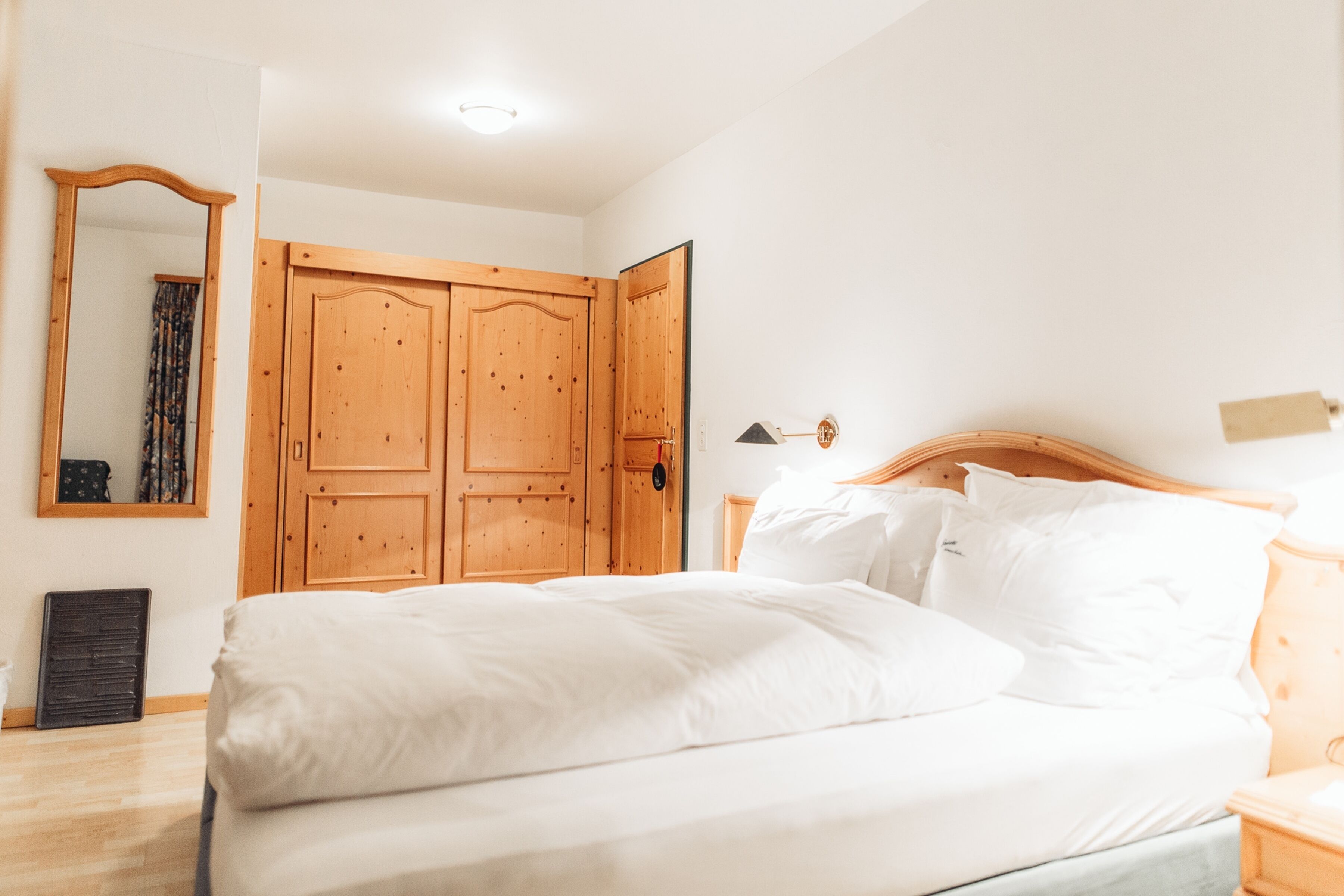 A bedroom with a wooden bed, a wardrobe, a mirror, and a bedside lamp.