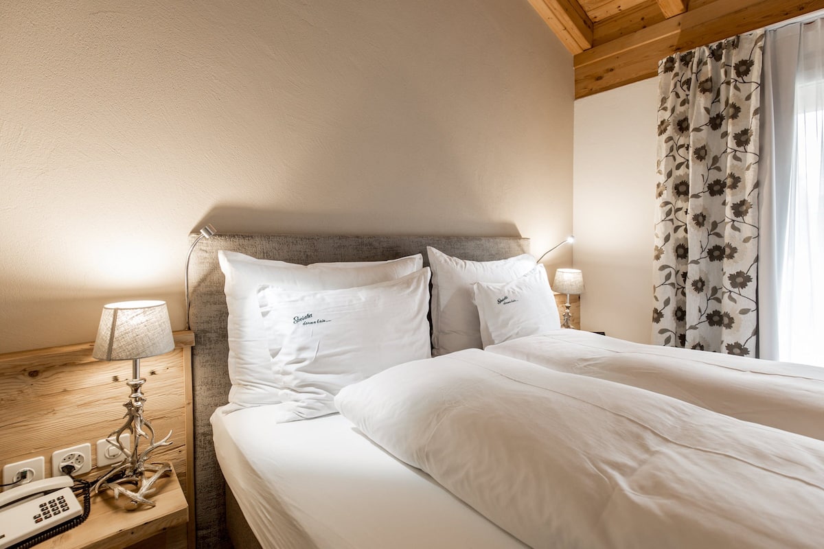Une chambre d’hôtel avec un lit, une lampe de chevet, un téléphone et une fenêtre ornée de rideaux à motifs floraux.