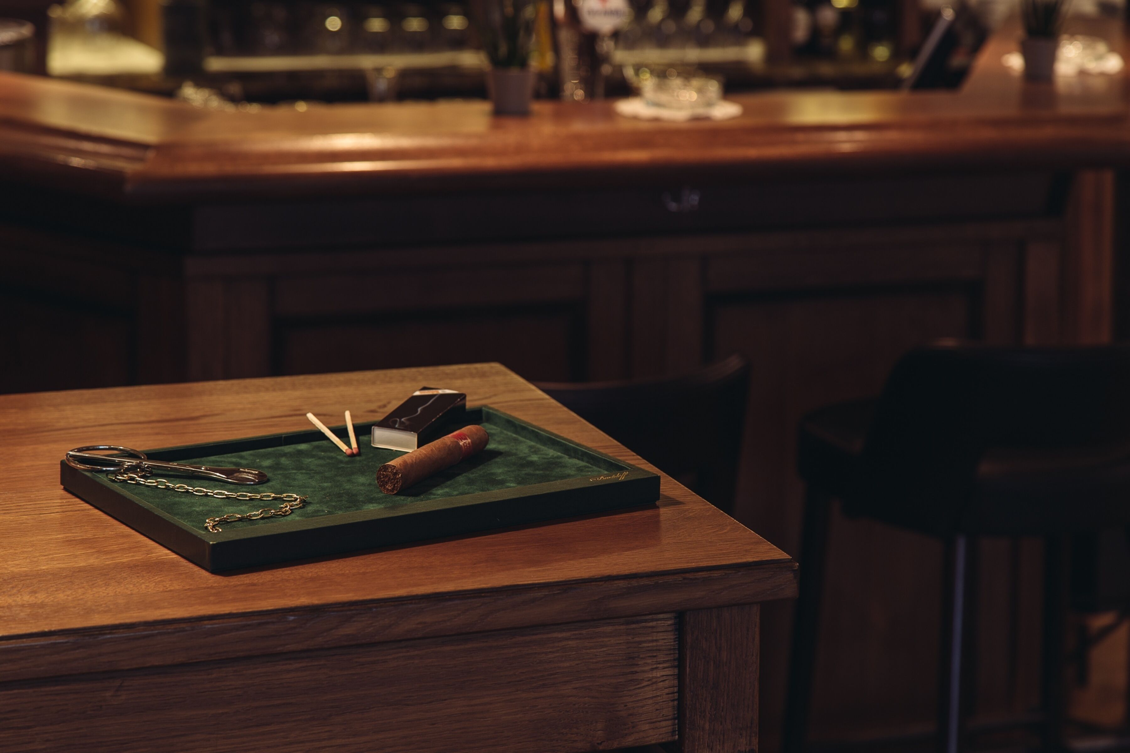 A bar area with a wooden counter and a green tray with a cigar, a lighter, and a box of matches.