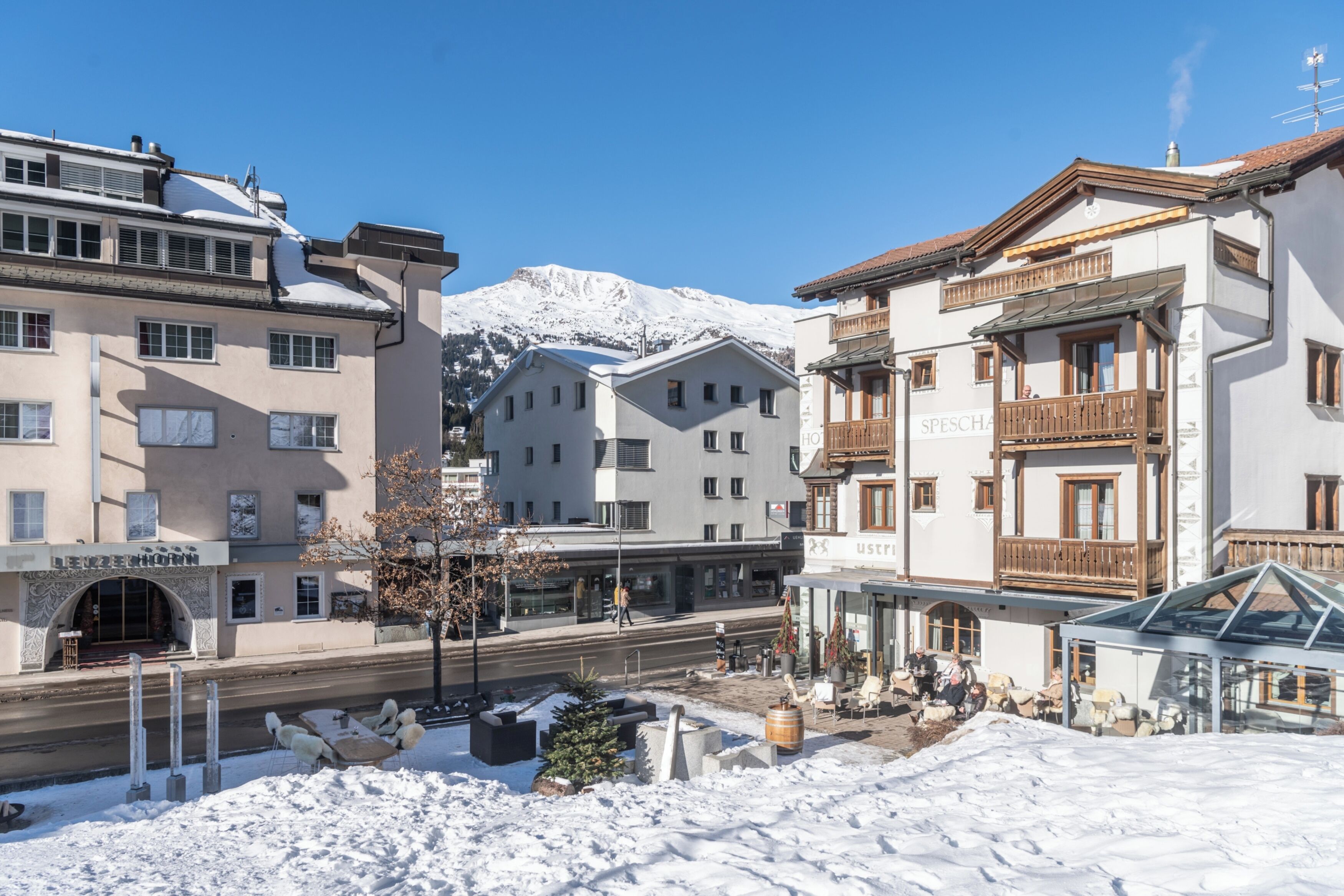 Un hôtel dont le sol est recouvert de neige, avec une montagne en arrière-plan et un ciel bleu dégagé.