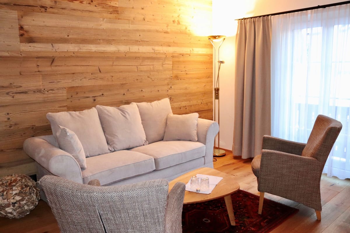 Un salon comprenant un canapé, deux fauteuils, une lampe sur pied et une fenêtre avec des rideaux.