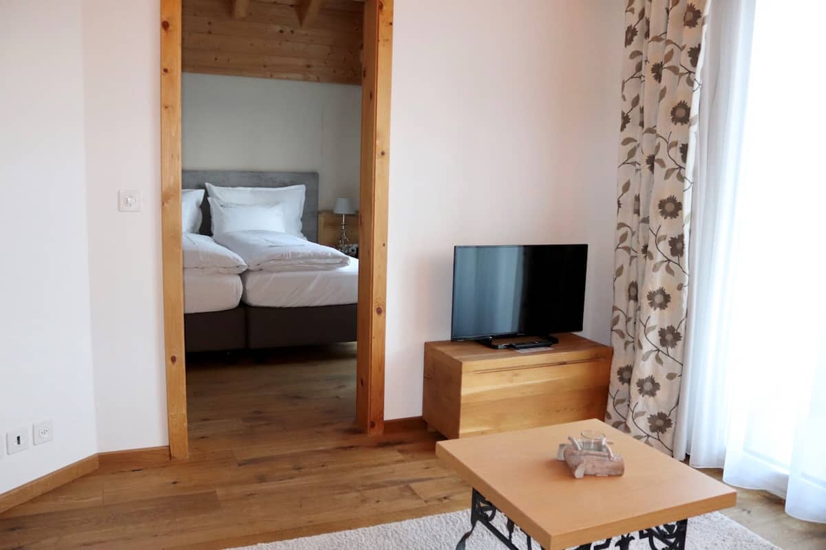 Une chambre à coucher avec un lit, un téléviseur posé sur un meuble en bois et une fenêtre ornée de rideaux à motifs floraux.