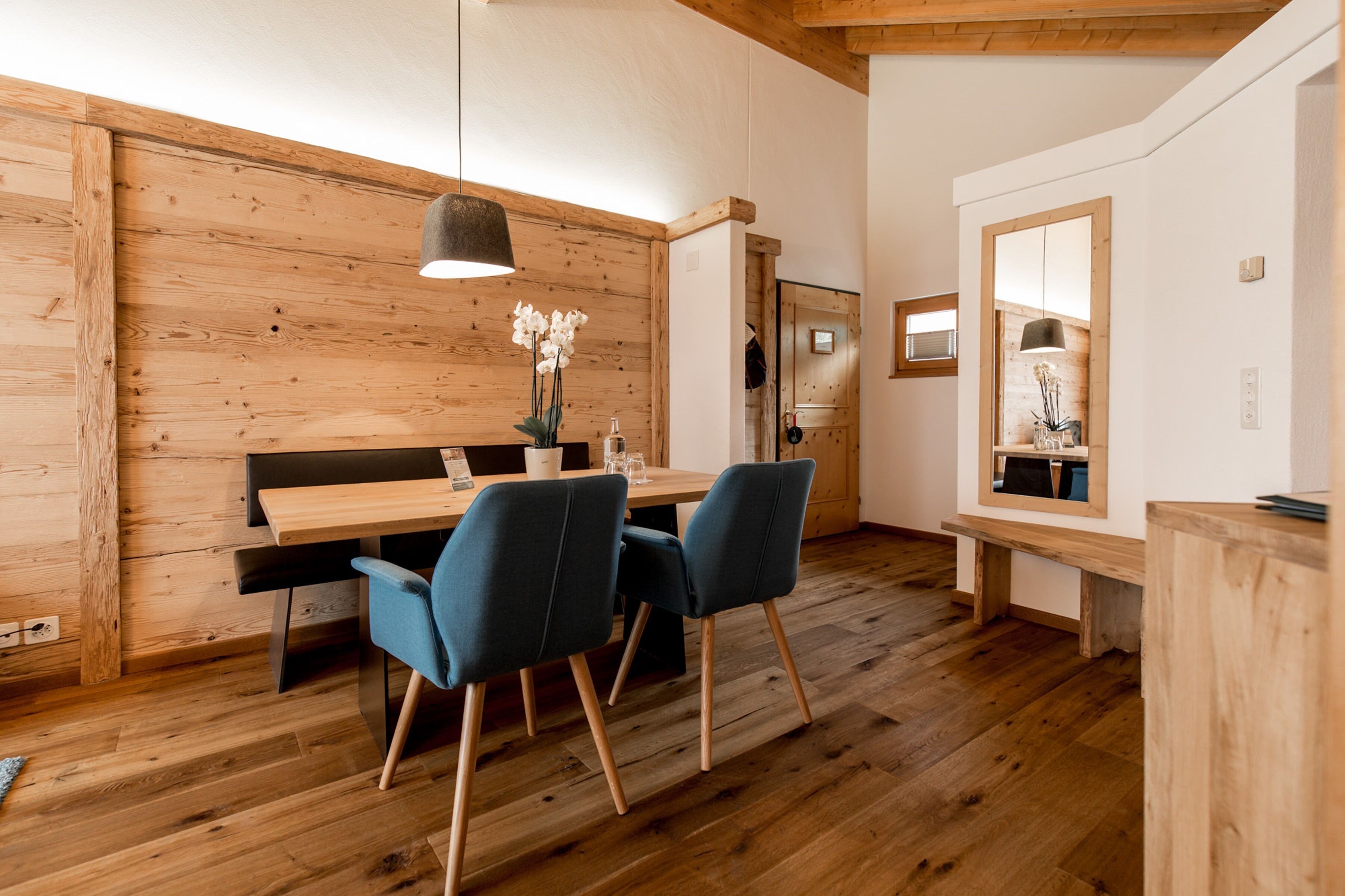 Una habitación moderna con paredes y suelos de madera, una mesa de comedor de madera con sillas azules, un banco y un espejo.