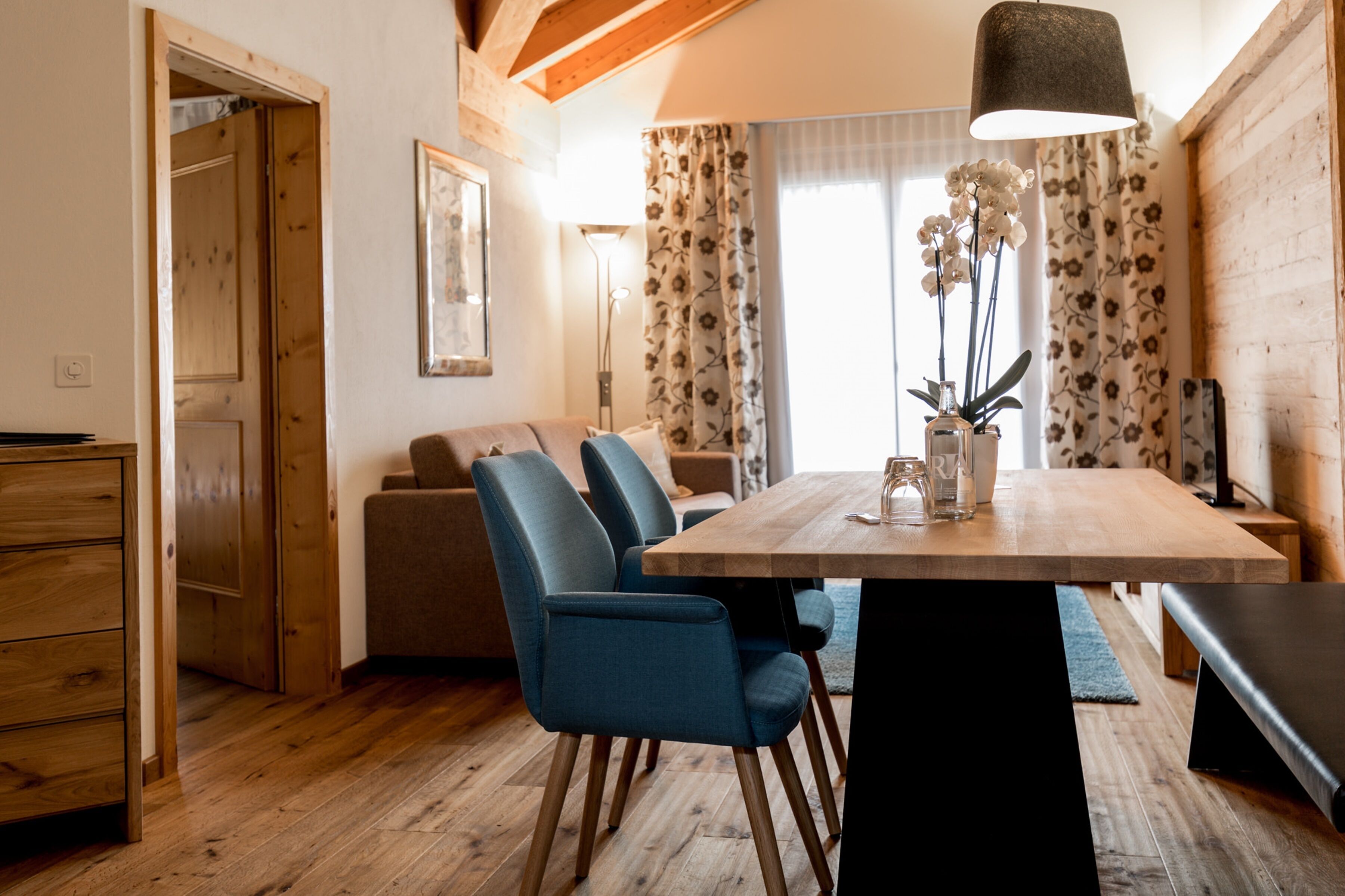 A dining area with a wooden table, blue chairs, and a hanging lamp.