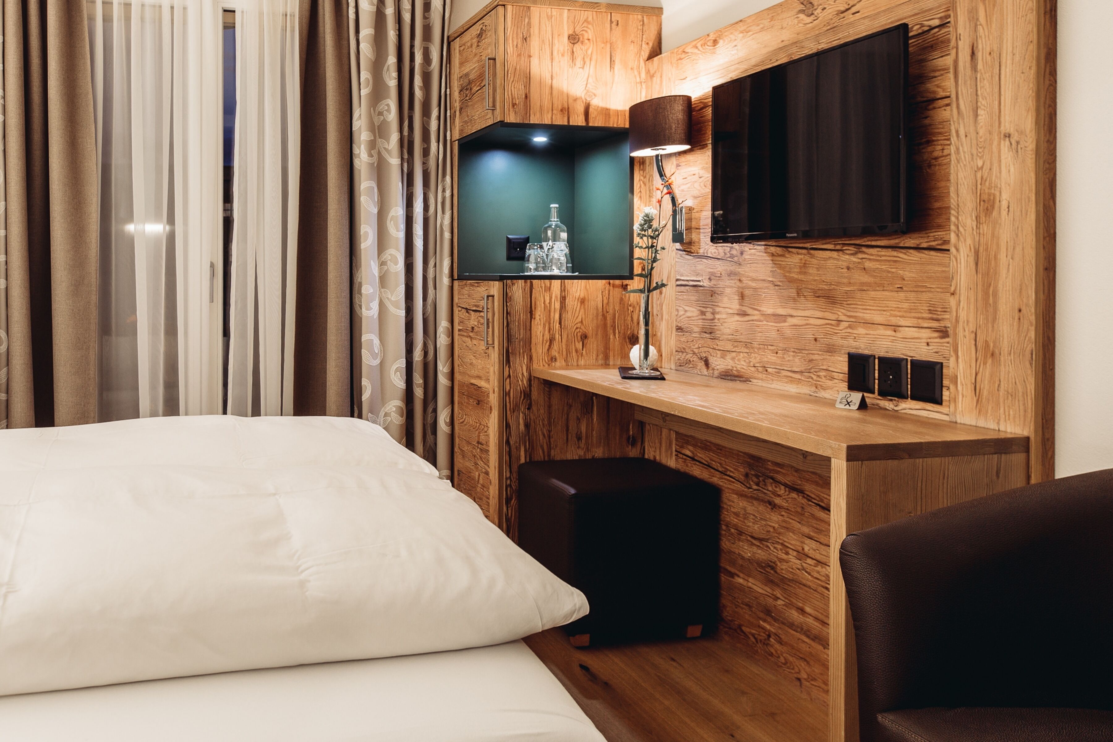 Ein modernes Hotelzimmer mit einer Wandvertäfelung aus Holz, einem Flachbildfernseher, einem Nachttisch mit Lampe und einem großen Bett mit weißer Bettwäsche.