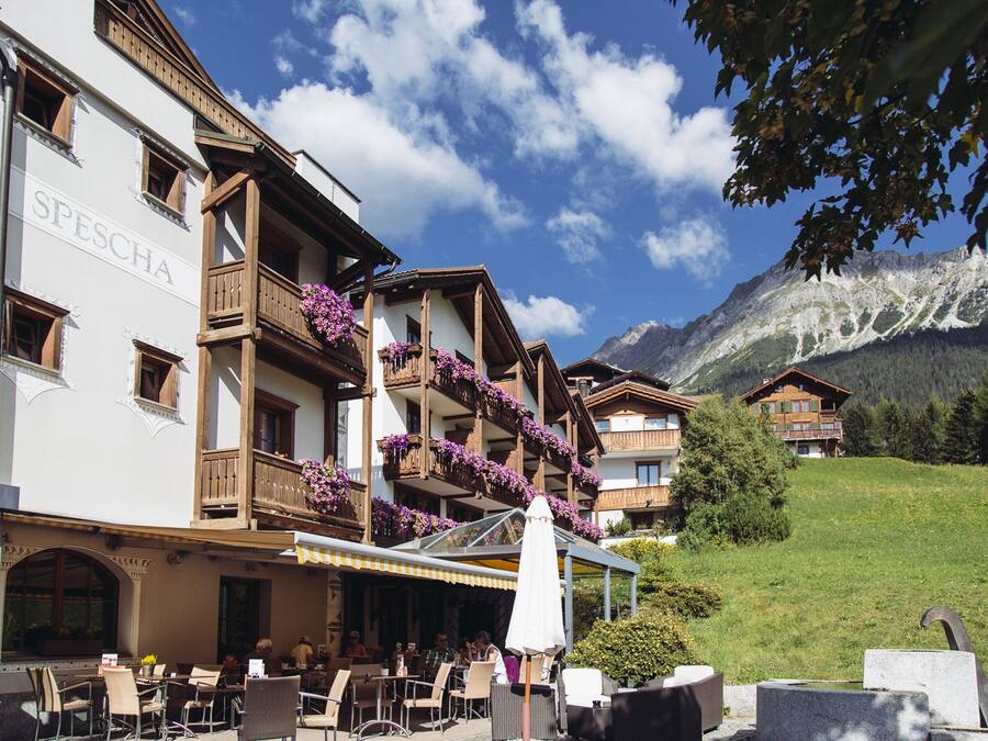 Un hotel con terraza al aire libre, balcones de madera y un paisaje de montañas al fondo.