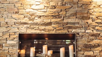 A stone wall with a metal fireplace shelf holding several candles.