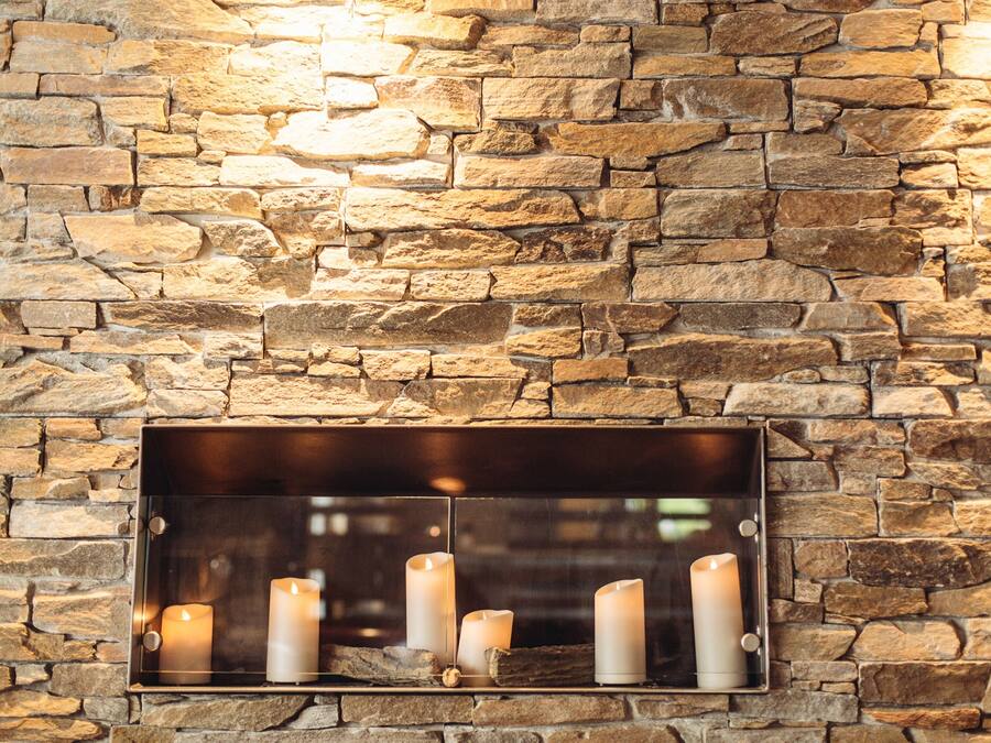 A stone wall with a metal fireplace shelf holding several candles.