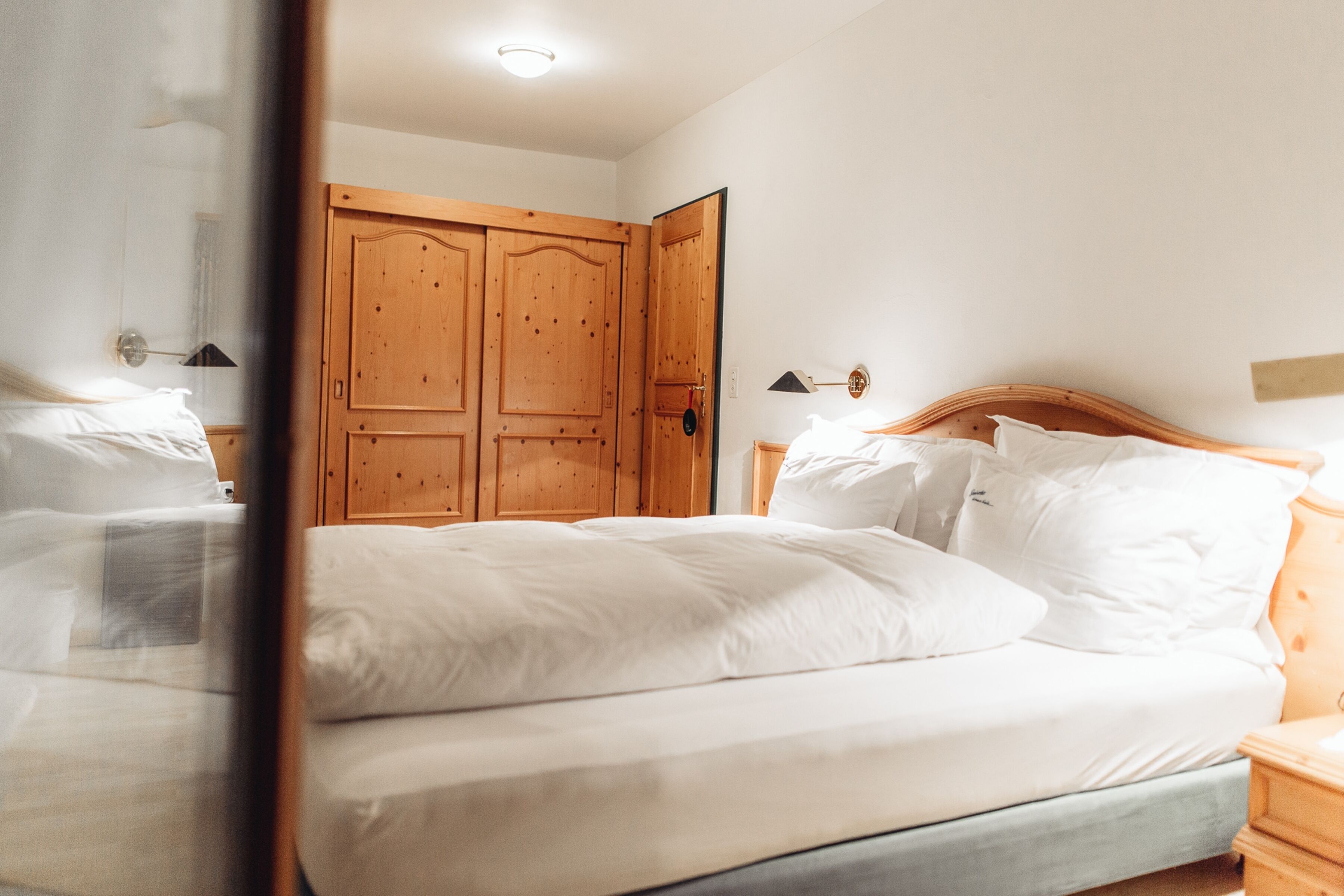 A bedroom with a bed, wooden wardrobe, and bedside lamps.