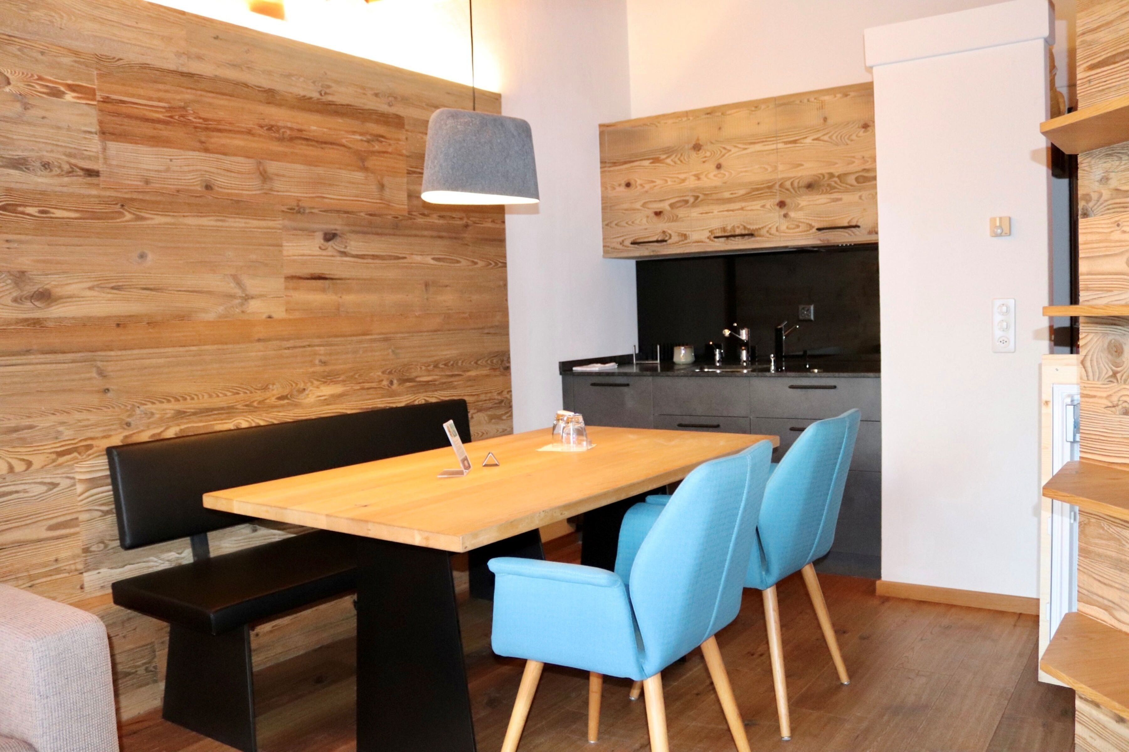 A modern kitchen with wooden accents, a dining table with blue chairs, and a bench.