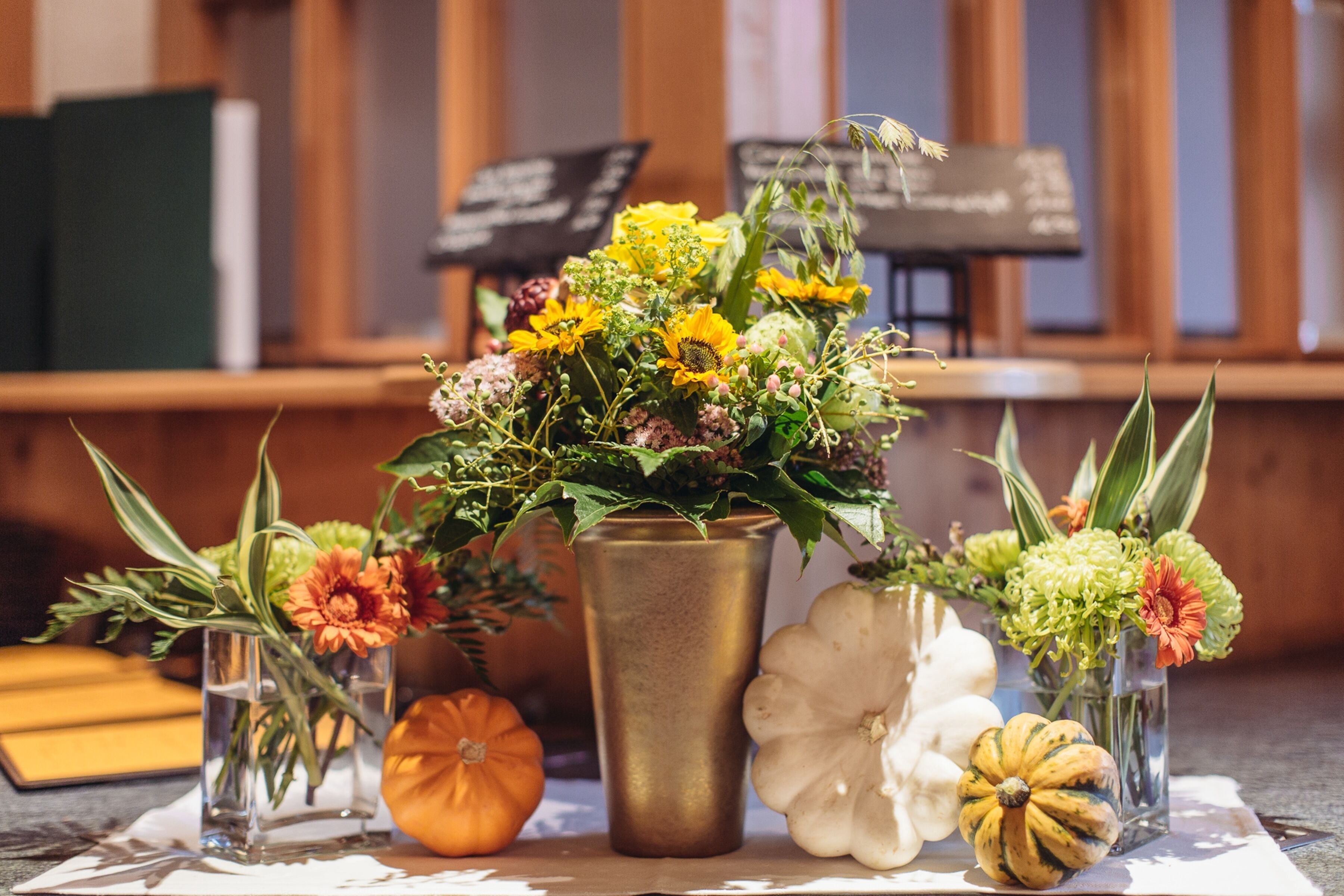 Una mesa con diversas flores y calabazas en jarrones de vidrio transparente.