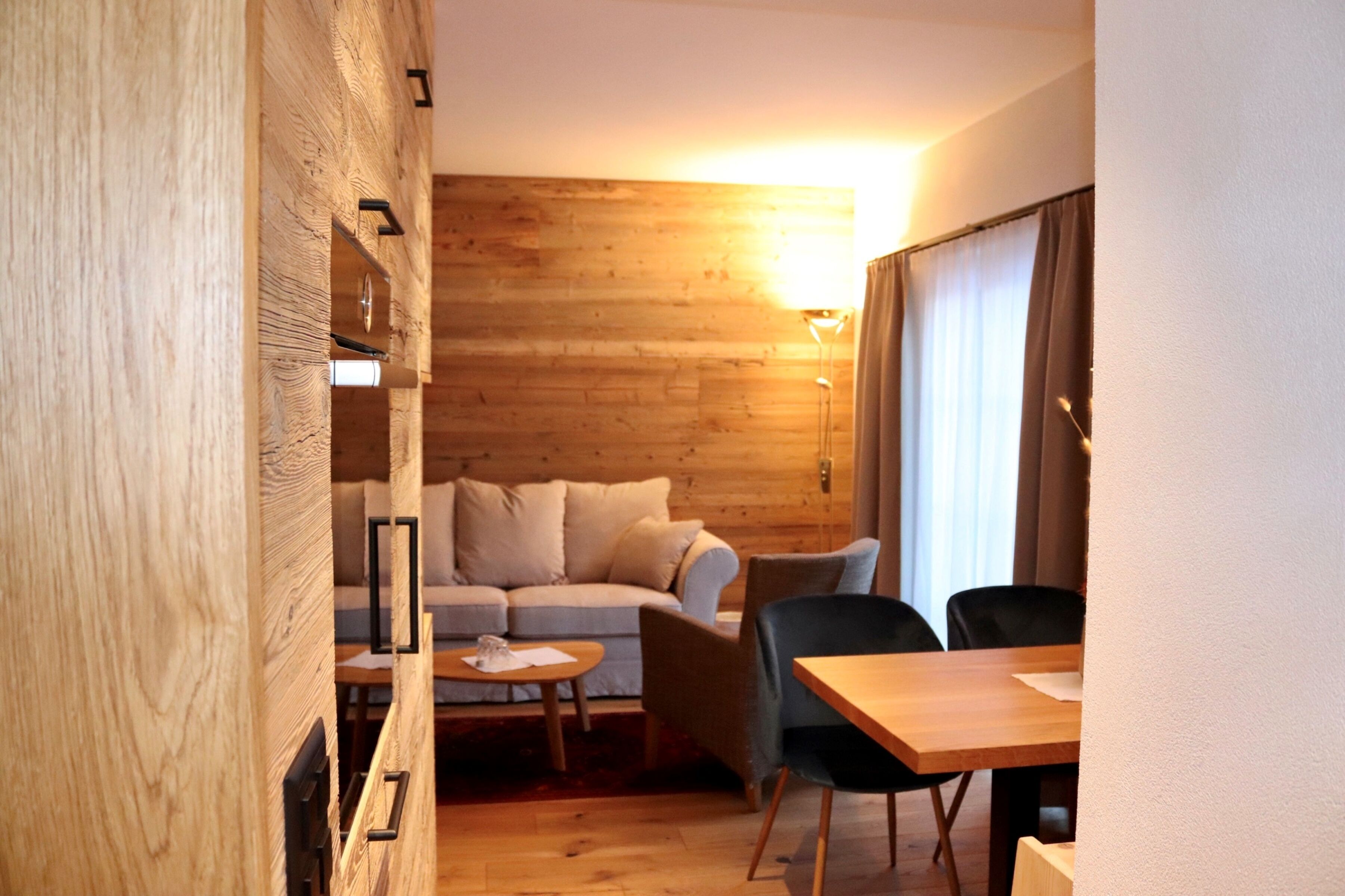 A cozy room with a wooden wall, a sofa, a small table, and a dining area with chairs.