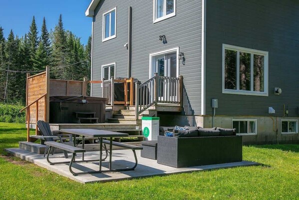 A two-story house with a covered patio area, outdoor seating, and a staircase leading to the upper floor. - Access to Lake Memphremagog - Spa - Constellation (Canton de Stanstead)
