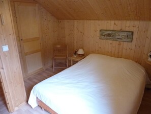 A wooden room with a bed, a chair, a nightstand, and a painting on the wall. - 3-star chalet with large terrace in lush setting (Le Biot)