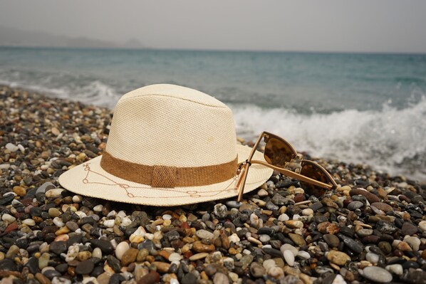 A straw hat and sunglasses on a pebbled beach with the ocean in the background. - Theros All Suite Hotel - Adults Only (Kos)