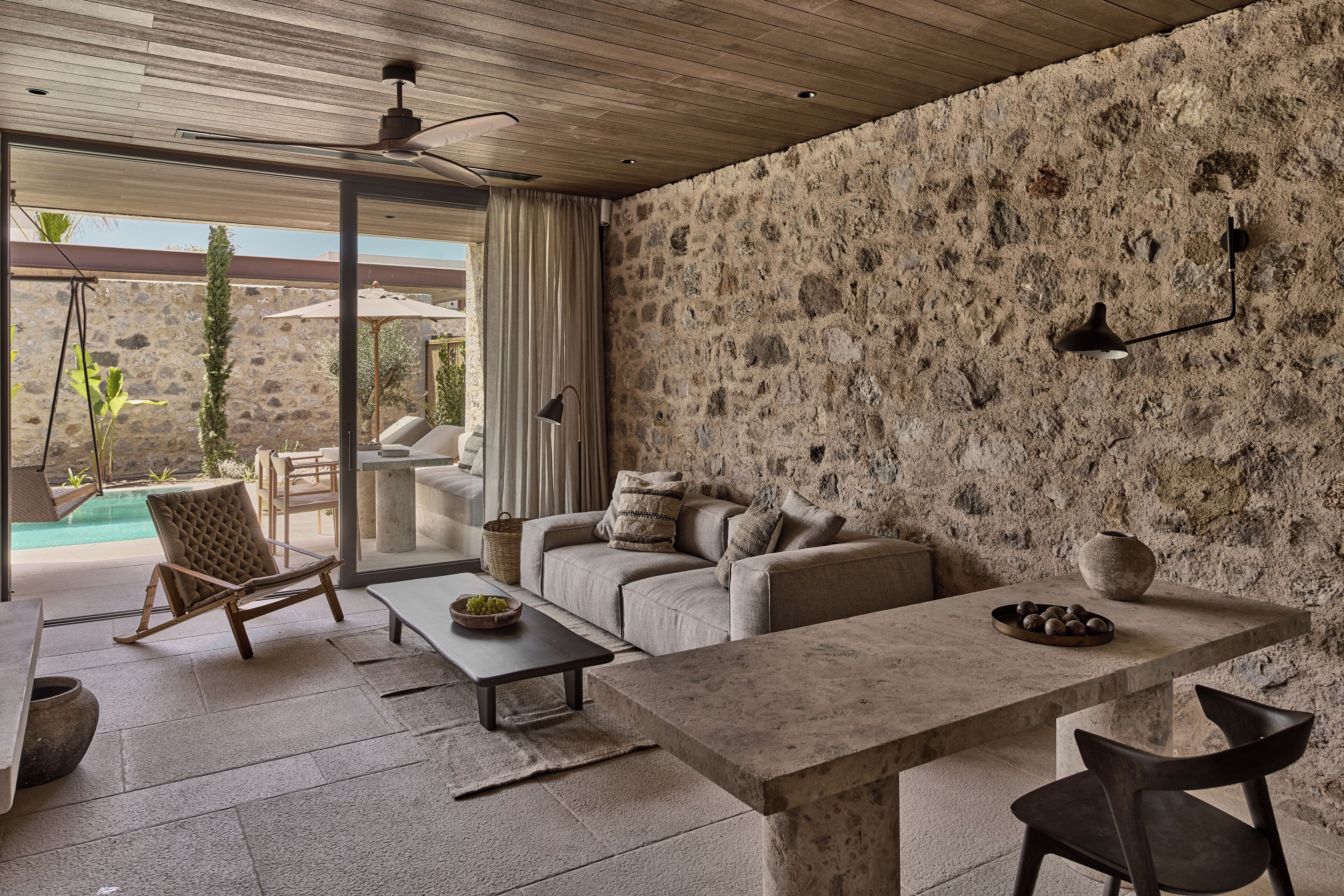 A modern living room with a stone wall, a sofa, a coffee table, and a dining table.