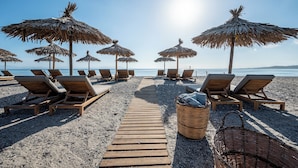 A beach with wooden lounge chairs and thatched umbrellas, a wooden walkway, and a beachside view. - Theros All Suite Hotel - Adults Only (Kos)