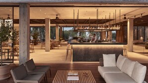 A spacious indoor area with a bar, seating arrangements, and large windows offering views of the outdoors. - Theros All Suite Hotel - Adults Only (Kos)