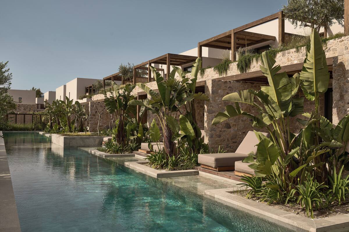 Un moderno complejo turístico con piscina, mobiliario exterior y abundante vegetación.