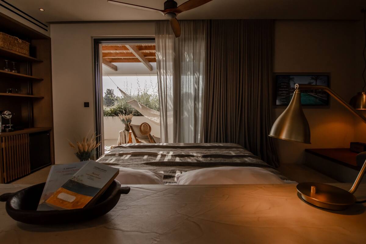 Un dormitorio moderno con una cama grande, una mesita de noche con lámpara, una estantería y una ventana con cortinas.