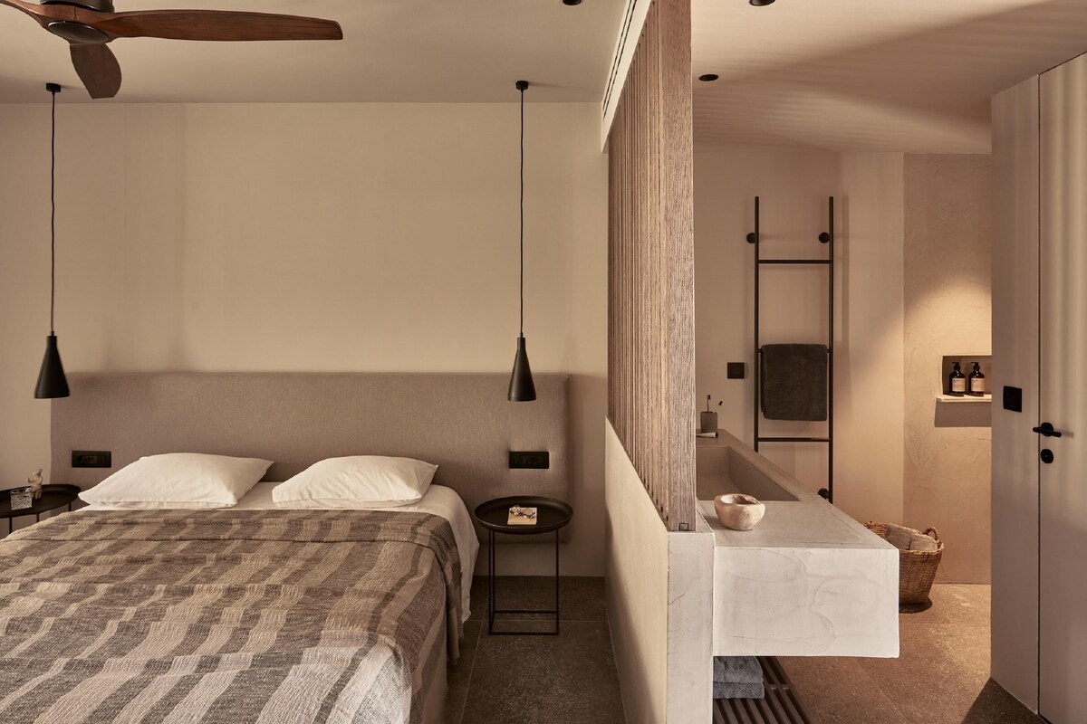 A modern bedroom with a bed, bedside tables, a ceiling fan, and a bathroom with a sink and mirror.