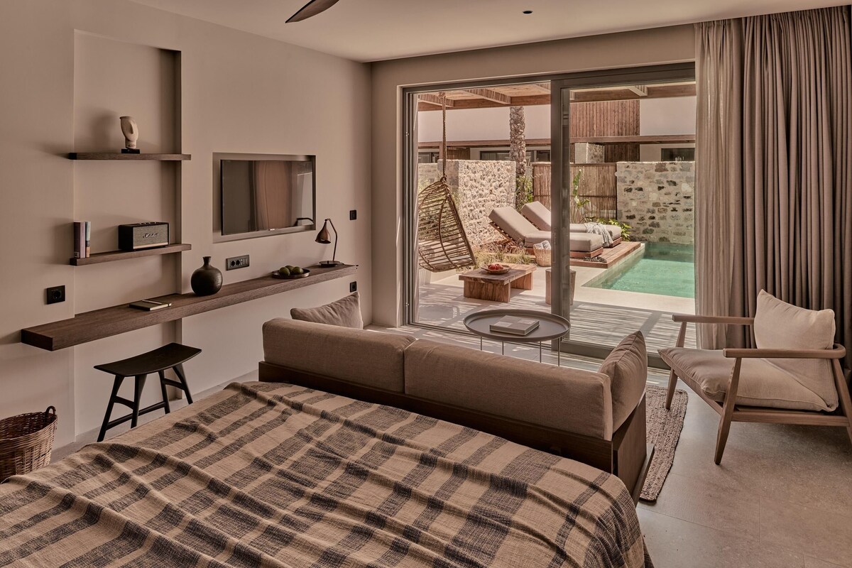 A modern hotel room with a large bed, a TV, a desk, and a view of an outdoor pool area.