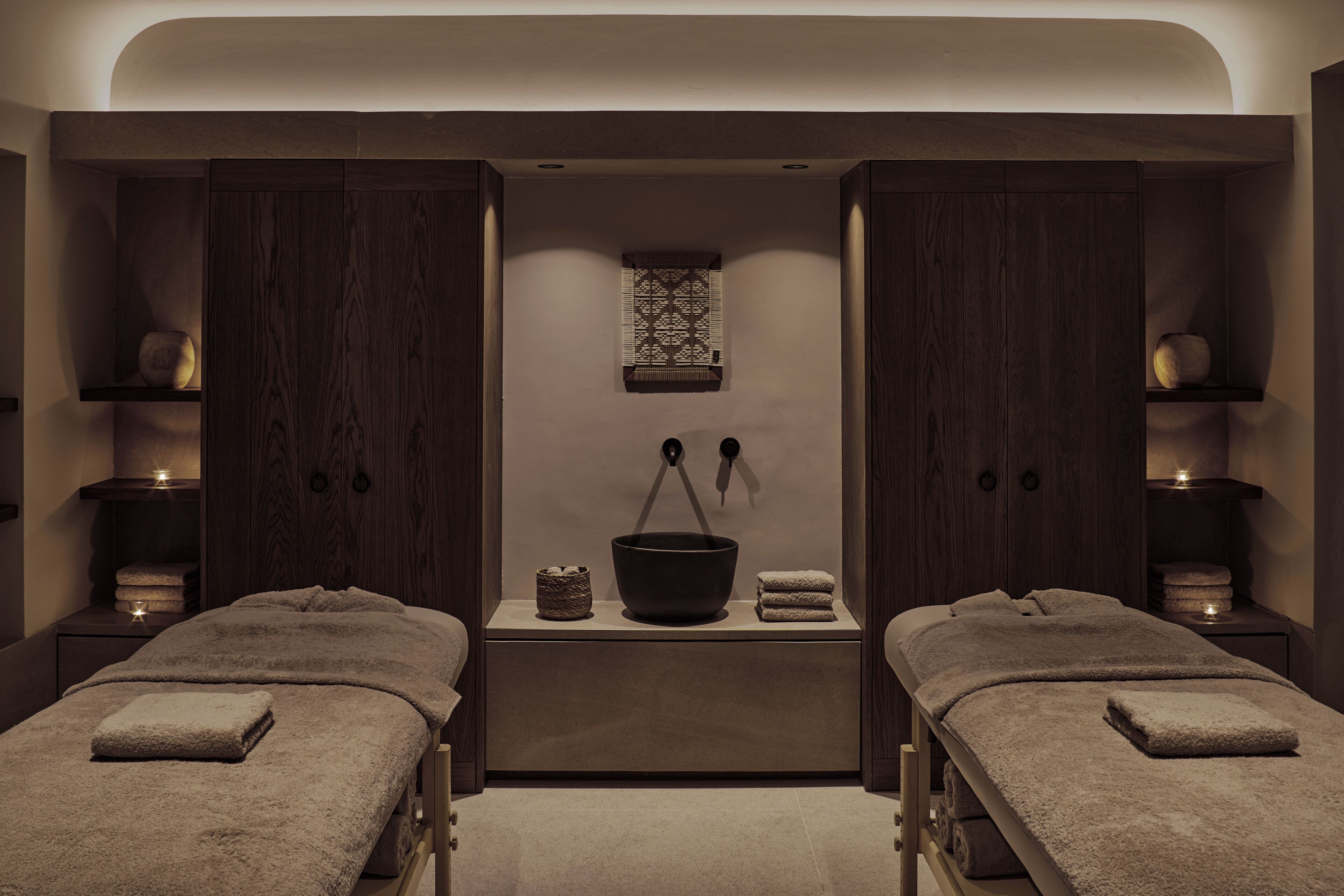 A spa room with two massage tables, a central basin, and wooden cabinets.