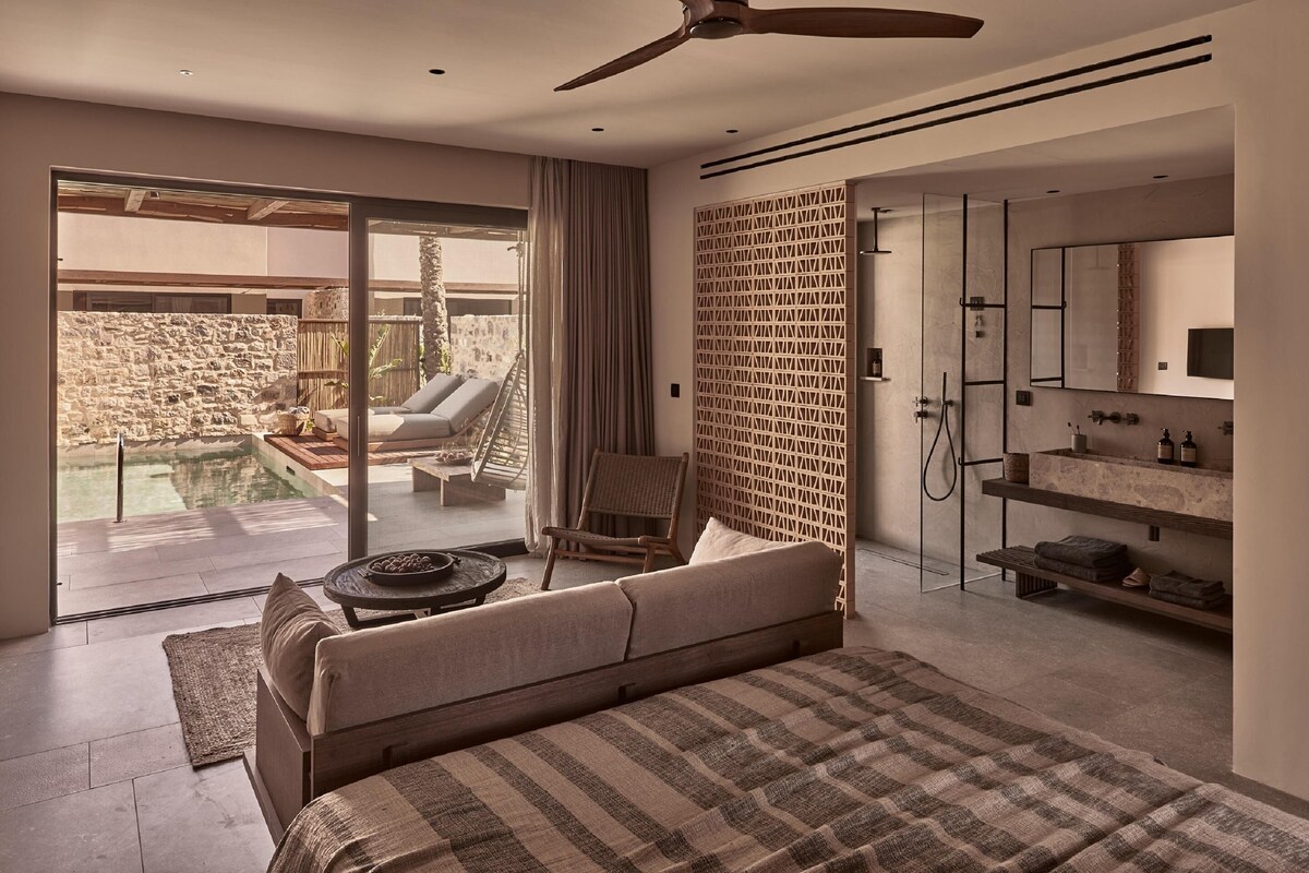 A modern bedroom with a large bed, a balcony with a pool, and a separate bathroom with a shower and sink.