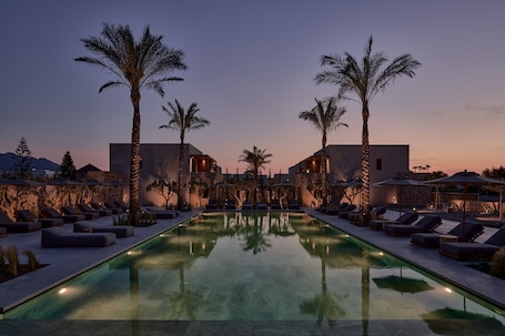 A pool area with lounge chairs and umbrellas, surrounded by palm trees and modern buildings.