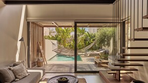 A modern living room with a sofa, a coffee table, and a view of an outdoor pool area. - Theros All Suite Hotel - Adults Only (Kos)