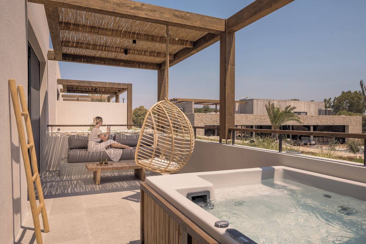 Un espacio exterior moderno con un jacuzzi, una silla colgante de madera y un sofá bajo una pérgola.