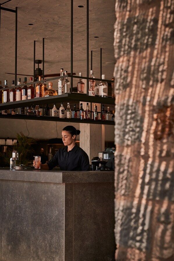 A bar area with shelves of bottles and a person preparing a drink. - Theros All Suite Hotel - Adults Only (Kos)