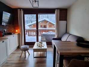 A modern living room with a wooden dining table, a sofa, and a TV mounted on the wall. - Modern apartment with large south-facing terrace, parking, TV and internet - 4 people (Châtel)