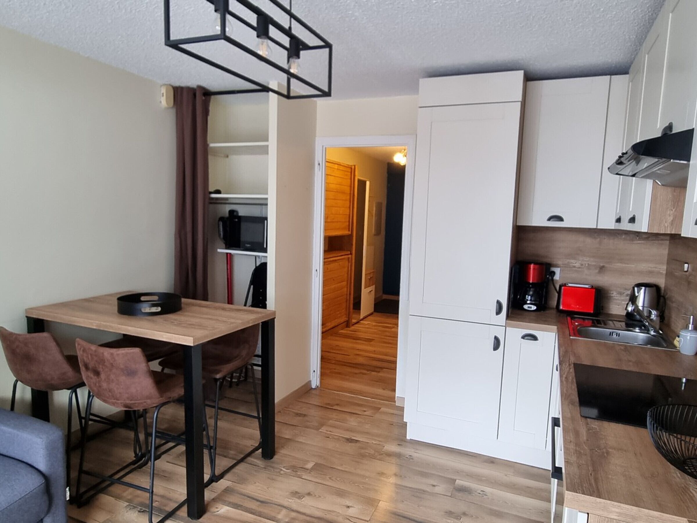 A compact kitchen with white cabinets, a wooden dining table, and a coffee machine.