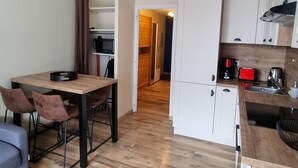 A compact kitchen with white cabinets, a wooden dining table, and a coffee machine.