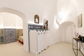 A room with a white wall, a tiled backsplash, a white cabinet with star decorations, a small table with a vase, and a framed picture. - Qasar Luxury Suite in Capri's Piazzetta (Capri)