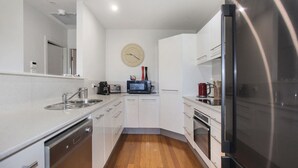 A compact kitchen with a microwave, toaster, and kettle on the countertop, a sink, and a clock on the wall. - 3 The Pier on The Myall River (Tea Gardens)