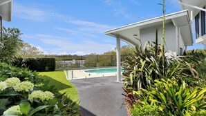 A modern house with a covered patio, a swimming pool, and lush greenery. - 3 The Pier on The Myall River (Tea Gardens)