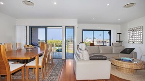 A modern living room with a dining area, a sofa, and a view of the outdoors. - 3 The Pier on The Myall River (Tea Gardens)