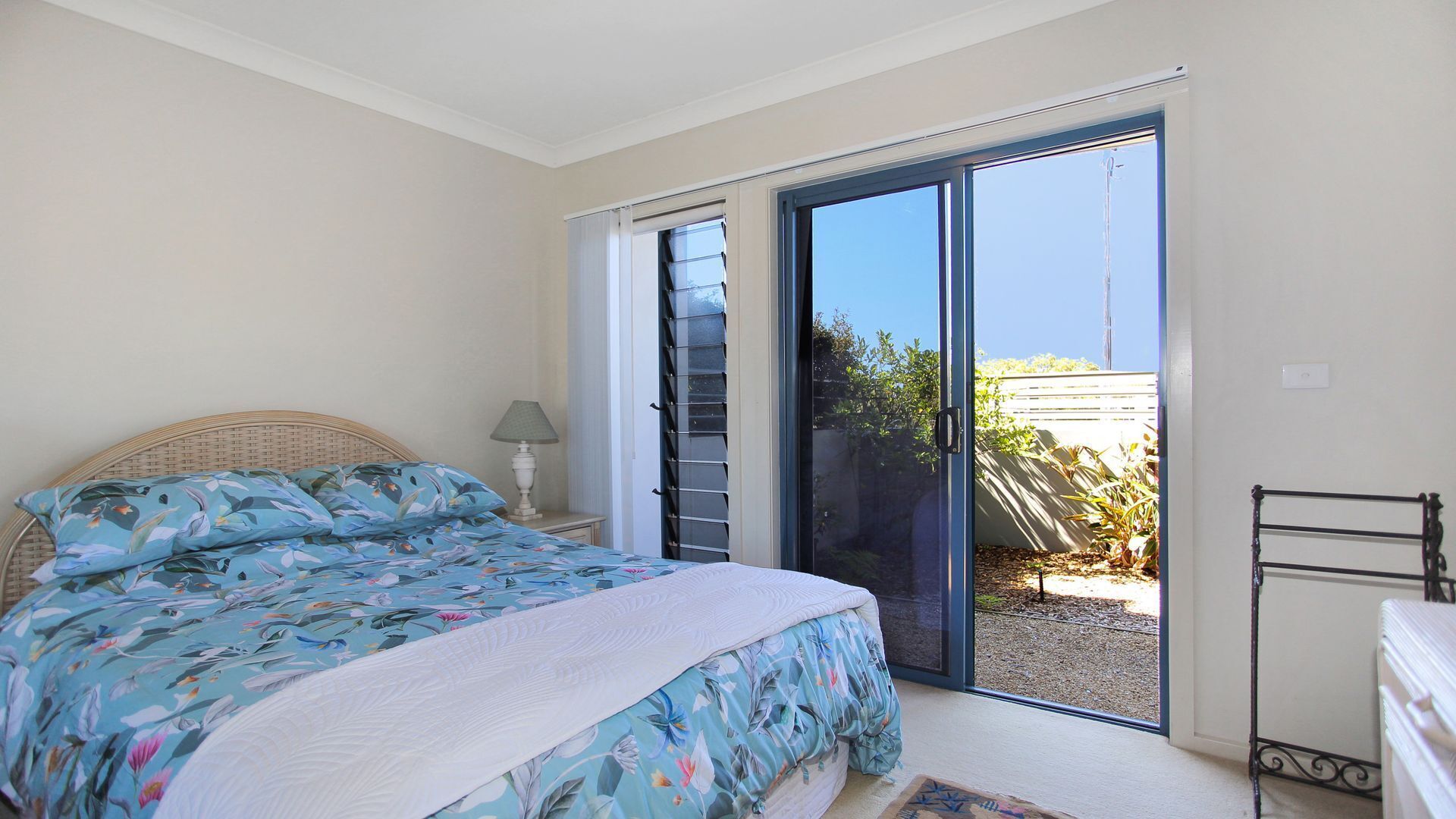 A bedroom with a bed, a nightstand, a lamp, a sliding glass door, and a view of the outside.