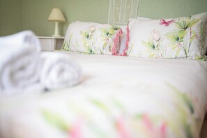 A neatly made bed with floral bedding and a pillow with a butterfly design. - The Enclave - Lake Tarawera Views, Sleeps 6 (Rotorua)