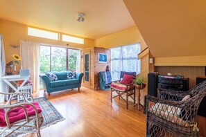 A spacious living area with a teal sofa, a wicker chair, and a small table with a plant. - The Enclave - Lake Tarawera Views, Sleeps 6 (Rotorua)