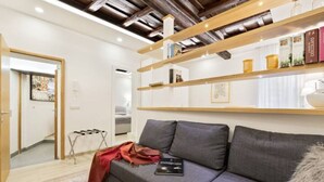 A modern living room with a grey sofa, wooden shelves, and a small table with a book. - Ciancaleoni Studio Atelier of the Artist - Monti (Roma)