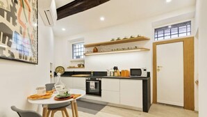A modern kitchen with white cabinets, a black countertop, a microwave, and a stove. There is a dining table with chairs and a small rug on the floor. - Ciancaleoni Studio Atelier of the Artist - Monti (Roma)