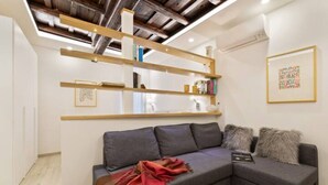 A modern living room with a grey sectional sofa, wooden shelves, and a framed artwork on the wall. - Ciancaleoni Studio Atelier of the Artist - Monti (Roma)