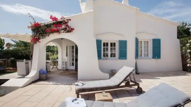 Un edificio blanco con persianas azules, un porche cubierto y una silla de descanso.