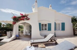 Un edificio blanco con persianas azules, un porche cubierto y una silla de descanso.