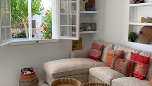 Una sala de estar moderna con un sofá blanco, dos sillones de mimbre, un ventilador de techo y un ventanal con vistas a zonas verdes.