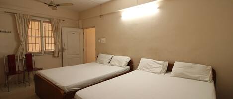 A room with two single beds, a ceiling fan, a window with curtains, and a desk with a chair.