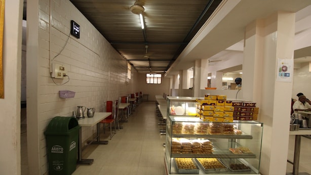 A bakery with a display case of baked goods, a trash bin, and a long counter with chairs. - Sibi Lodge (Coimbatore)